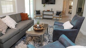 Ein modernes Wohnzimmer mit grauem Sofa, blauen Sessel und Couchtisch. Ein Flachbildfernseher ist an der Wand befestigt.