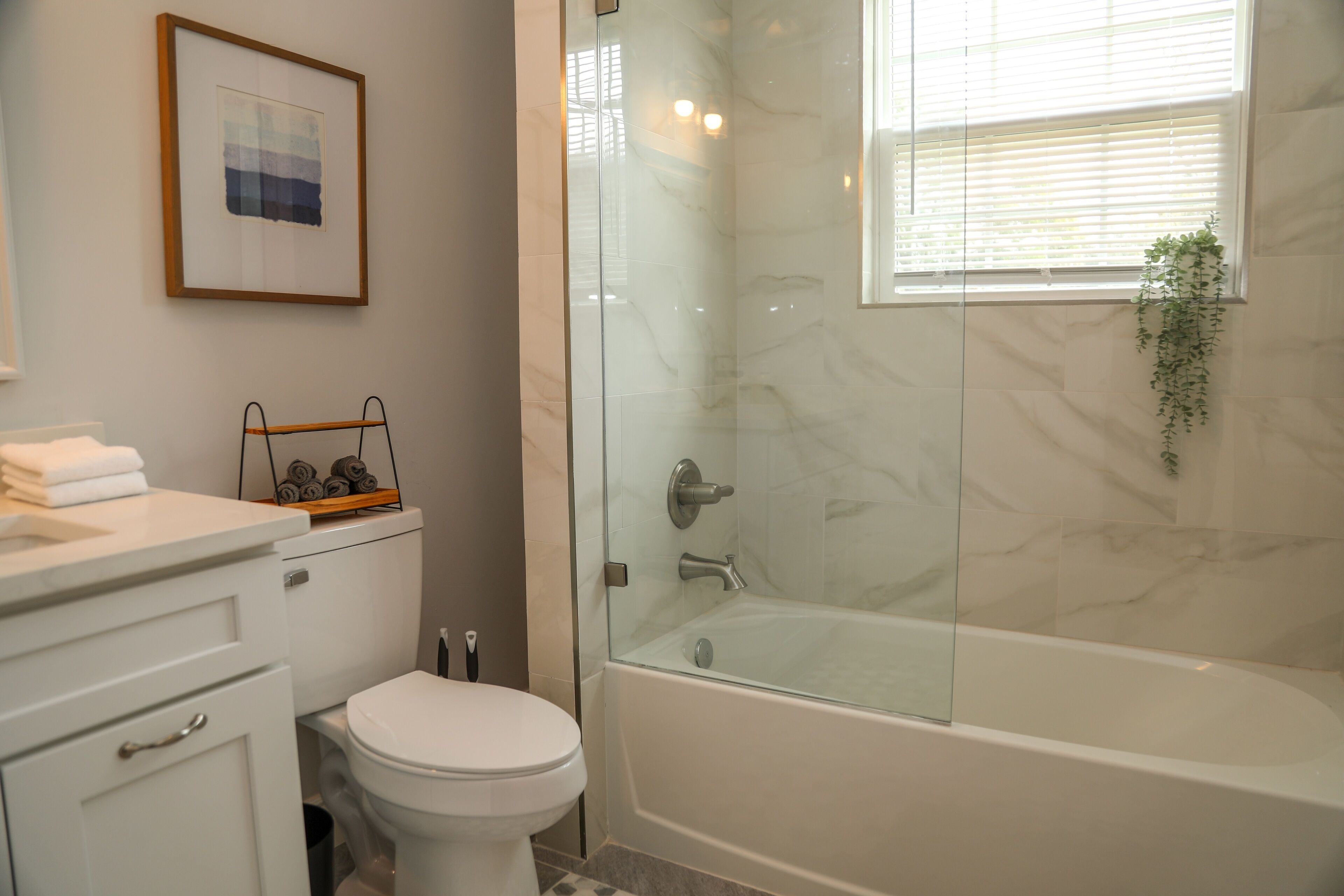 Ein Badezimmer mit einer gläsernen Duschkabine, einer weißen Toilette, einer Wand mit Marmorplatten und einem gerahmten Bild.