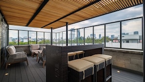 Eine Dachterrasse mit Korbmöbeln, großen Fenstern und Blick auf die Skyline der Stadt.