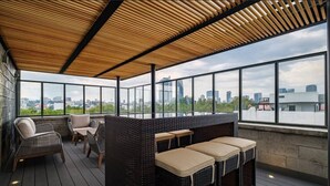 A rooftop terrace with wicker furniture, large windows, and a city view.