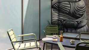 A modern outdoor seating area with metal chairs and a table, a large abstract mural on the wall, and a potted plant.