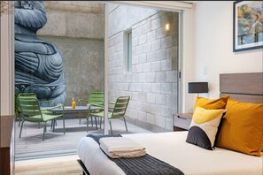 Moderni hotellihuone, jossa on sänky, pieni pöytä tuoleineen, suuri seinämaalaus ja ikkuna.