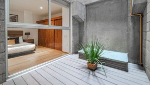 A modern bedroom with a sliding glass door leading to a balcony, a potted plant, and a visible bathroom.