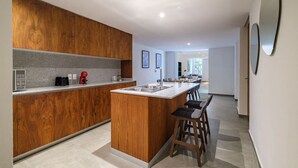 A modern kitchen with wooden cabinetry, a central island with bar stools, and a view into the adjacent living area.