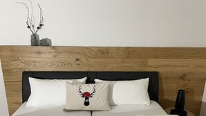 Ein Bett mit weißer Bettwäsche, einem Holz-Kopfbrett und zwei Kissen, eines mit einem Hirsch-Motiv.