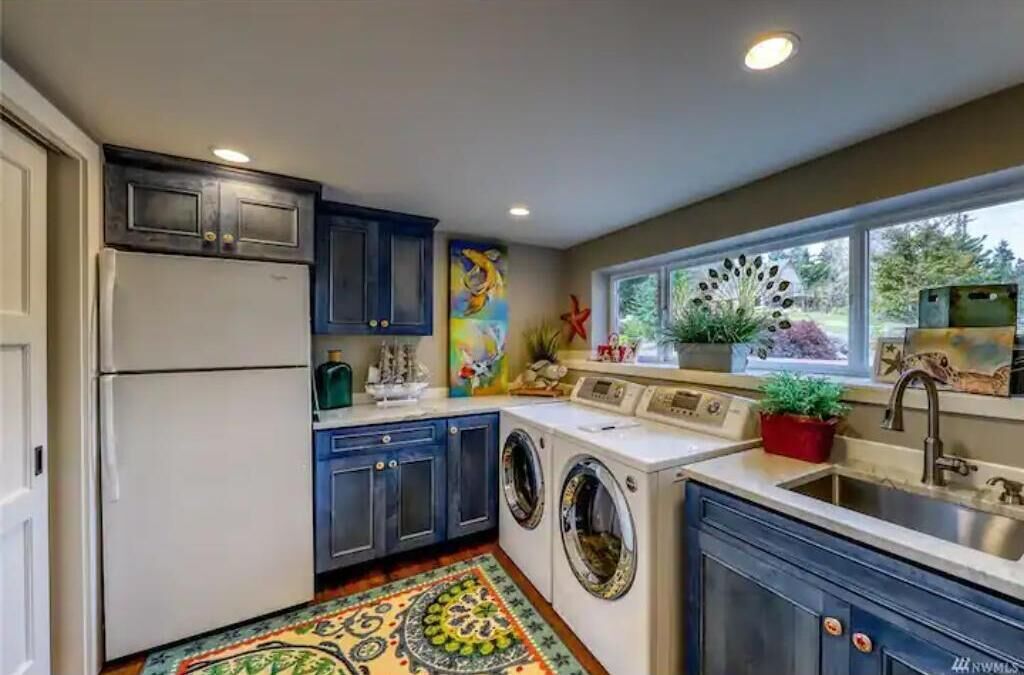 Une cuisine compacte équipée d’un réfrigérateur, d’un lave-linge et d’un évier. Une fenêtre offre une vue sur la verdure environnante.