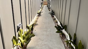 A long, narrow corridor with a concrete floor, flanked by vertical walls with air conditioning units. - OceansideLuxuryCondo*Walk2Beach*Pool*Pets*NoStairs (Corolla)