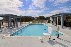 En rektangulär swimmingpool med ett klart, blått vatten, omgiven av en kakelbeklädd poolterrass. På höger sida finns två vita solstolar och en vit poolstege.
