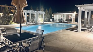 A pool area with lounge chairs, a table, and a covered seating area at night. - OceansideLuxuryCondo*Walk2Beach*Pool*Pets*NoStairs (Corolla)