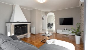 En moderne stue med pejs, sofa, fjernsyn og spiseplads, der kan ses gennem en bue.