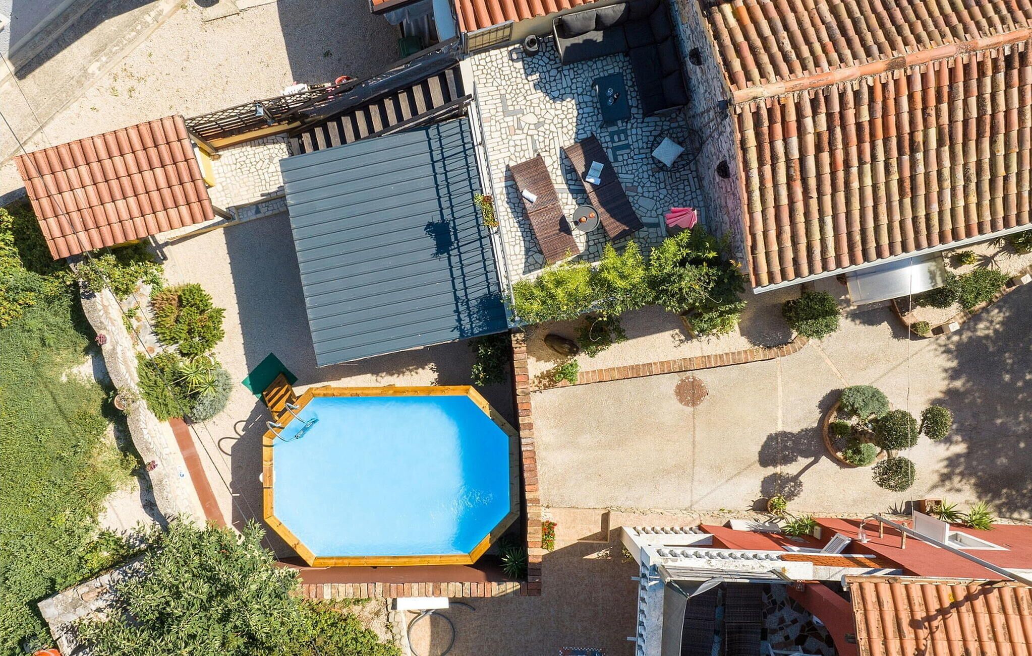An aerial view of a property with a swimming pool, a covered patio area, and a tiled roof.