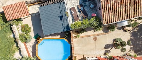 An aerial view of a property with a swimming pool, a covered patio area, and a tiled roof.