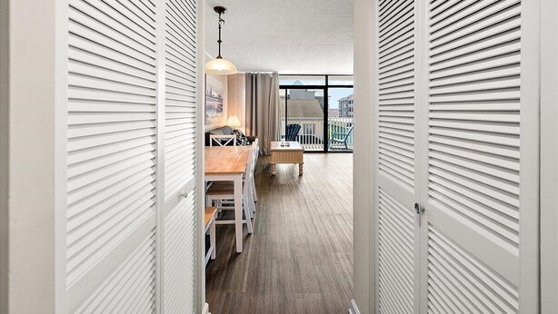 Un couloir doté d’un plancher en bois, de portes coulissantes blanches, d’un coin repas avec une table et des chaises, et offrant une vue sur les bâtiments à travers de grandes fenêtres.