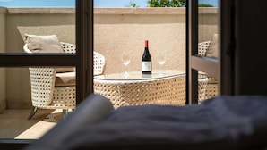 A balcony with wicker furniture, a glass table, and a bottle of wine.