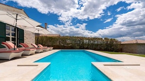 A rectangular swimming pool with clear blue water, surrounded by lounge chairs and umbrellas.