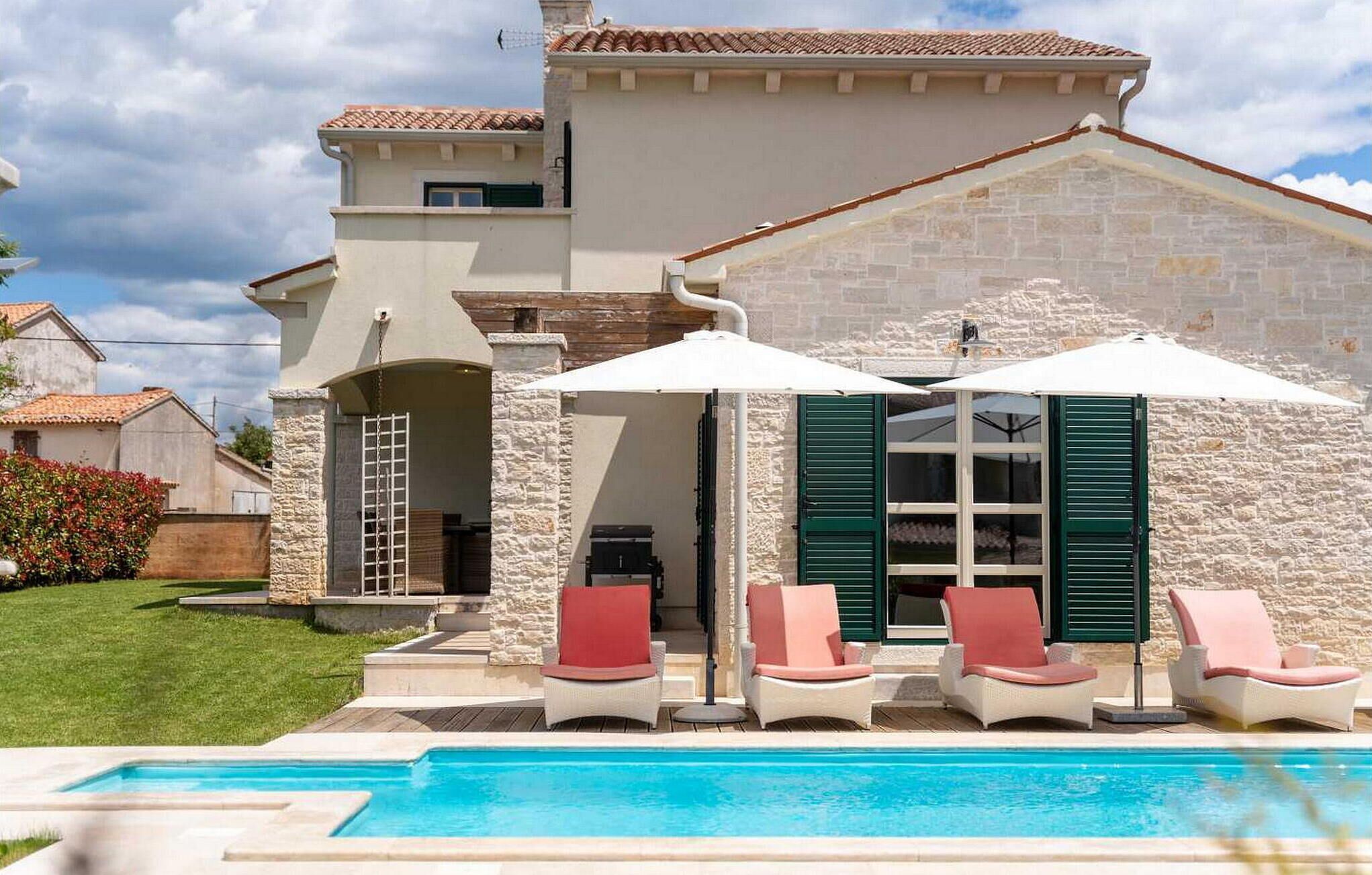 Una casa de dos pisos con piscina, mobiliario exterior y paredes de piedra.