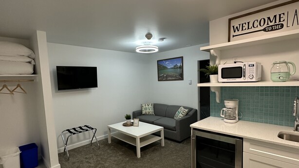 A compact living space with a kitchenette, a gray sofa, a flat-screen TV, and a coffee maker.