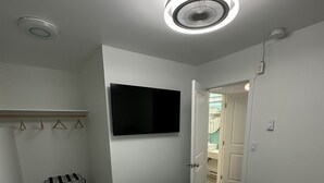 A bedroom with a bed, a TV mounted on the wall, a coat rack, and a door leading to another room.