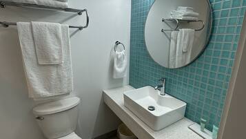 Een moderne badkamer met toilet, wastafel en spiegel. Handdoeken liggen op de handdoekhouder en er staat een prullenbak.