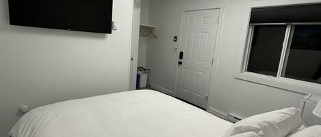 Ein Schlafzimmer mit einem großen Bett, einem an der Wand montierten Fernseher, einer Tür und einem Fenster.