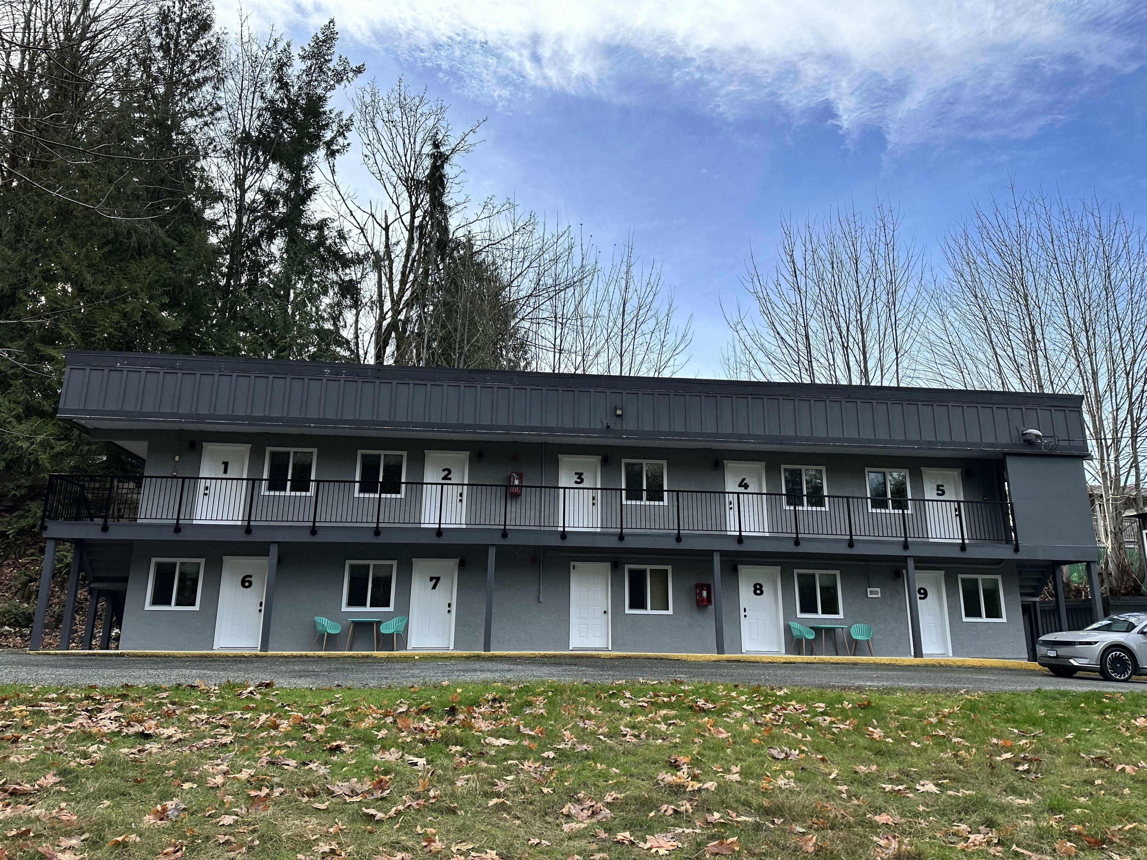 Un motel de dos pisos con habitaciones numeradas, asientos al aire libre y un estacionamiento.