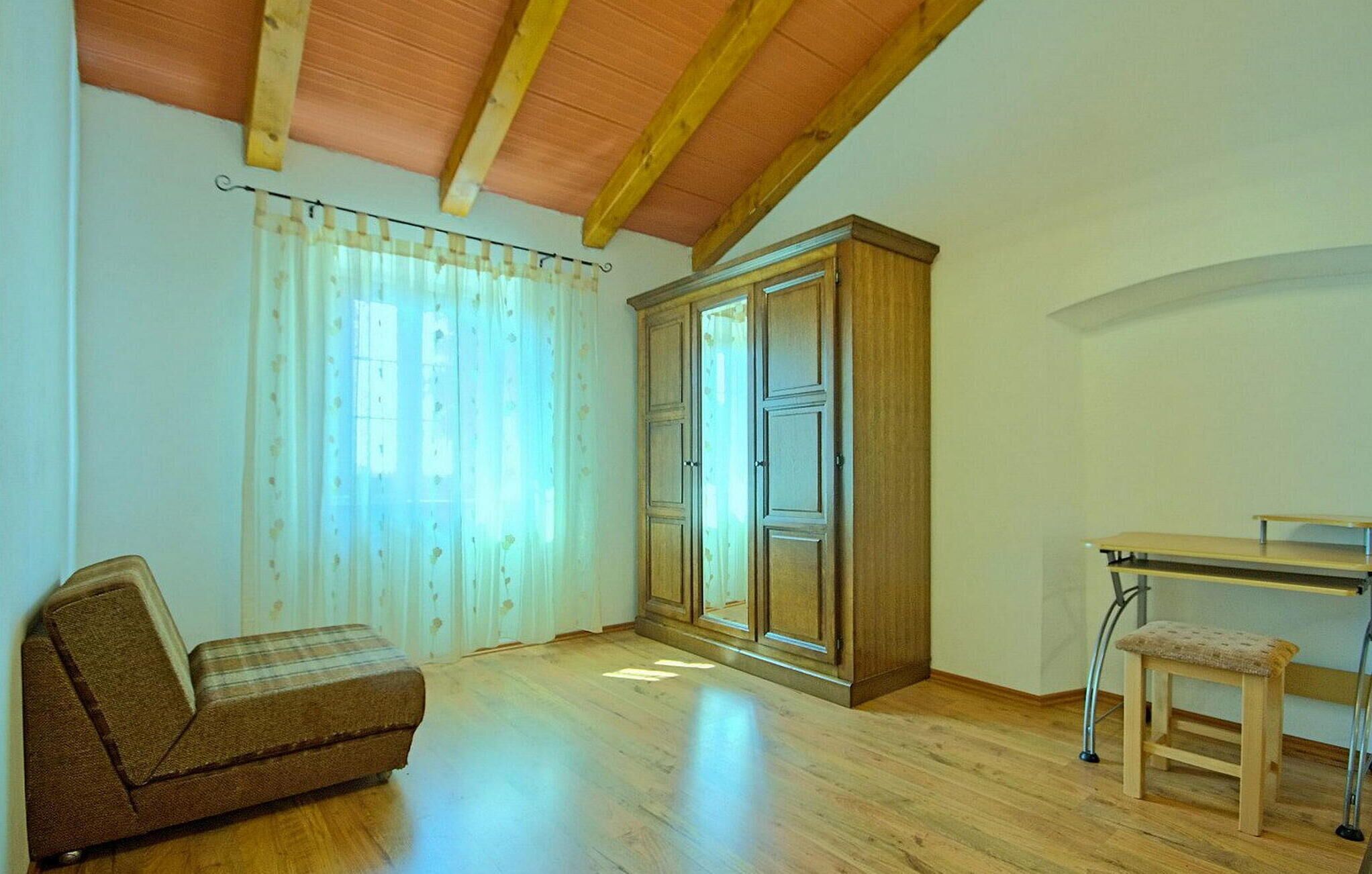A room with a wooden ceiling, a large wardrobe, a sofa, a small table, and a chair.