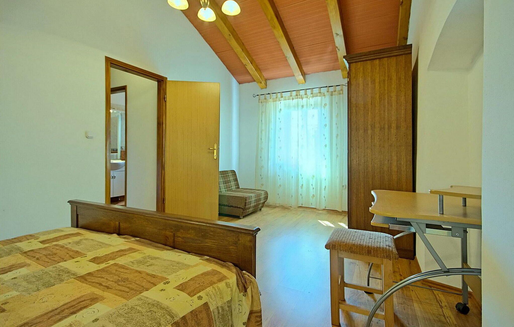 Une chambre à coucher avec un lit, un bureau, une chaise, un miroir et une fenêtre avec des rideaux.