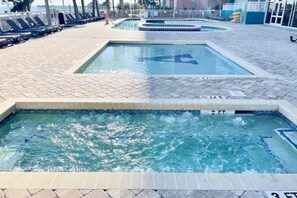 A swimming pool area with multiple pools, tiled walkways, and lounge chairs.