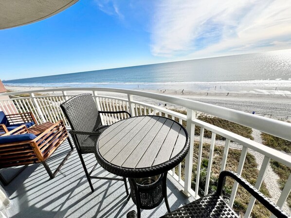 A deck with a round table and chairs, overlooking a beach.