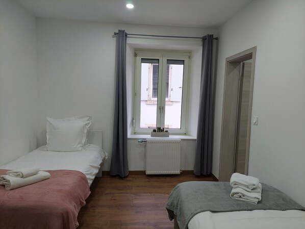A bedroom with two beds, a radiator, a window with curtains, and a door.