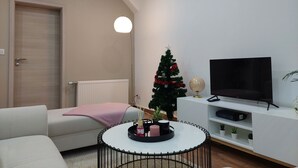 A living room with a white sofa, a small Christmas tree, a TV on a white stand, and a radiator. - Le Bag 3 chambres appartement familial (Colmar)