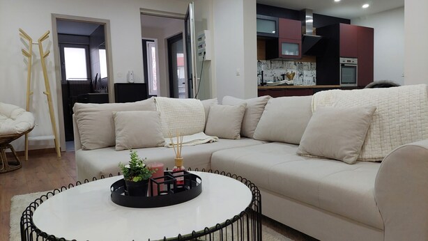 A modern living room with a white sofa, a round coffee table, and a kitchen area in the background. - Le Bag 3 chambres appartement familial (Colmar)