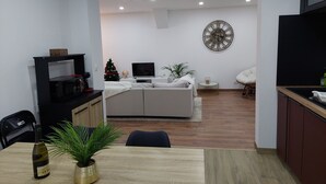 A modern living room with a sofa, TV, decorative wall clock, and a dining area with a table and chairs. - Le Bag 3 chambres appartement familial (Colmar)