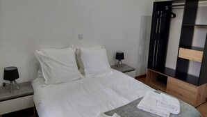 A hotel room with a bed, a nightstand, a lamp, a wardrobe, and a towel on the bed. - Le Bag 3 chambres appartement familial (Colmar)