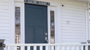 Una casa blanca con una puerta azul oscuro y un cartel que dice "ELECTRIC SUMMER".