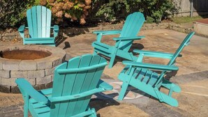 Un espacio al aire libre con tres sillas Adirondack color turquesa y un hogar de piedra.