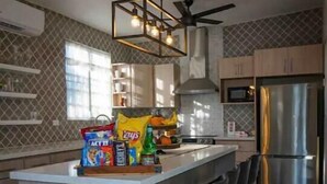 A modern kitchen with a central island, bar stools, a stainless steel refrigerator, and a ceiling fan. - Surfer Villa +Pool in Rincon’s Heart walk to Beach (Rincon)