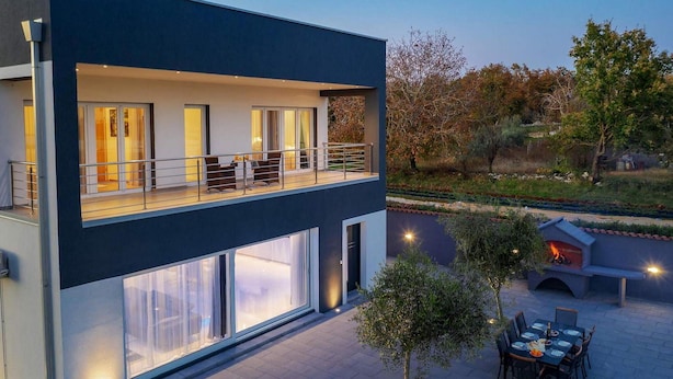 Un bâtiment moderne à deux étages, doté de grandes fenêtres, d’un balcon et d’un patio aménagé avec une table pour les repas.