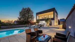 Une maison moderne à deux étages, dotée d’une piscine, de mobilier d’extérieur et d’un espace patio.