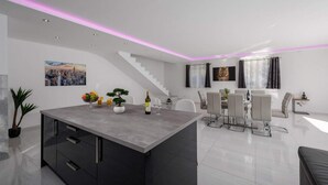 Une cuisine moderne dotée d’un îlot central, d’un coin repas avec des chaises et d’un escalier.