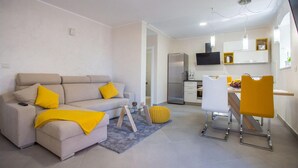 A modern living room with a sofa, coffee table, and chairs. There is a kitchen area with a refrigerator, microwave, and a TV mounted on the wall. - 2 bedroom beautiful home in Porec (Porec)