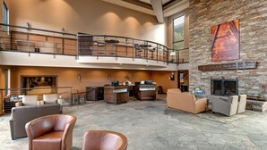 A spacious lobby with a high ceiling, a stone fireplace, leather seating, and a second-floor balcony with bar stools. - Comfortable Condo in Park City (Park City)