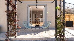 Een overdekt terras met twee blauwe metalen stoelen, een tafel en een hanglamp.