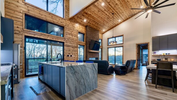 A modern kitchen with a marble island, wooden ceiling, and large windows. - All is Found Riverfront Cabin with Sauna (Broken Bow)