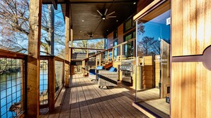 A wooden deck with a view of a lake, a grill, and a wicker chair. - All is Found Riverfront Cabin with Sauna (Broken Bow)