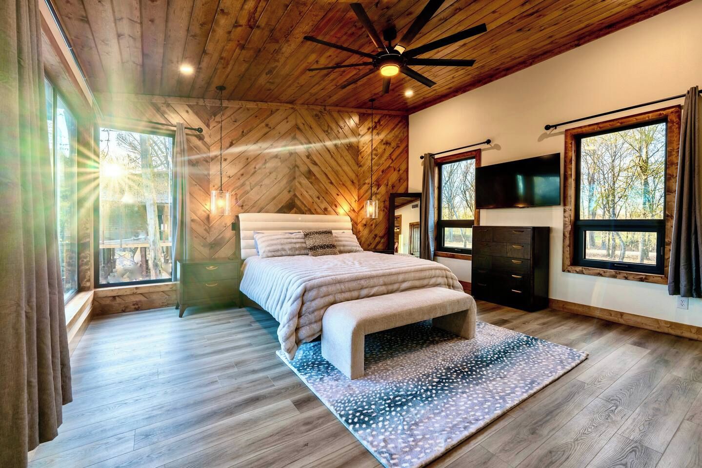A bedroom with a bed, a dresser, a television, and large windows.