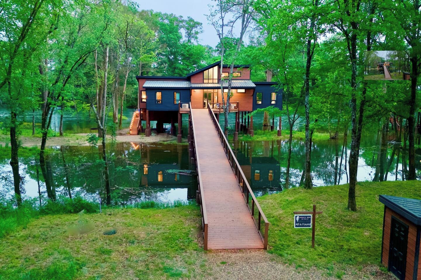 A house with a wooden deck leading to a dock over water, surrounded by trees.