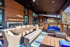 A covered outdoor area with a wooden deck, a dining table with chairs, a sofa, and a fireplace. - All is Found Riverfront Cabin with Sauna (Broken Bow)