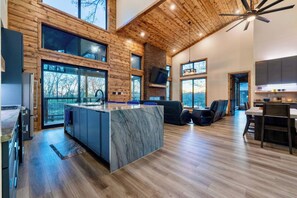 Una cocina moderna con una isla de mármol, piso de madera y grandes ventanales que ofrecen vistas al exterior.