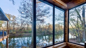 A cabin with large windows overlooking a lake and forest. - All is Found Riverfront Cabin with Sauna (Broken Bow)